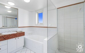 A bathroom with a white sink, a mirror, a bathtub, and a shower area.