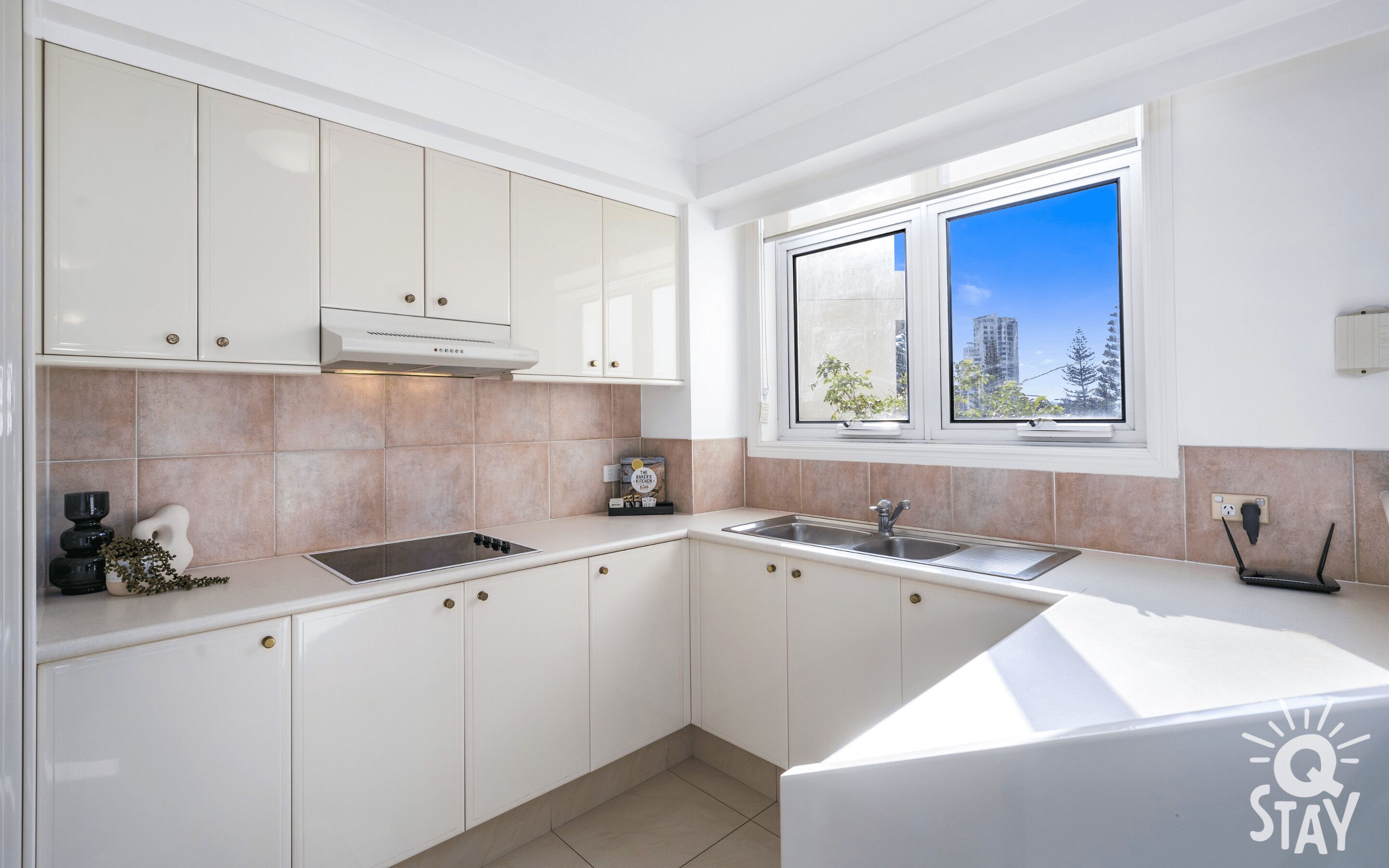 A modern kitchen with white cabinets, a built-in stove, a sink, and a window with a city view.