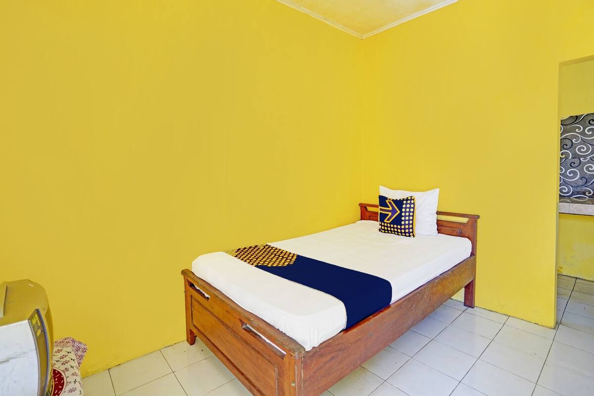 A single-bed room with a wooden frame, white bedding, and a yellow wall.