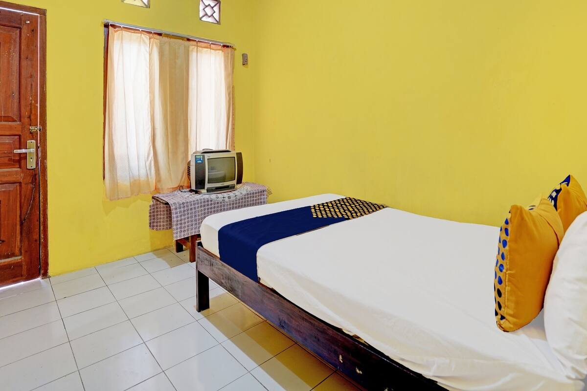 A bedroom with a bed, a television on a small table, and a window with curtains.