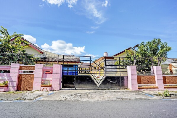 A gated entrance with a metal gate and a concrete pathway leading to a building with a red roof and a blue window. - SPOT ON 92372 Rinda Homestay Syariah & Resto (Banyuwangi)