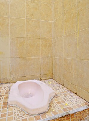 A bathroom with a pink toilet, tiled walls, and a patterned floor. - SPOT ON 92372 Rinda Homestay Syariah & Resto (Banyuwangi)