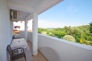 Un balcon avec une table et des chaises, donnant sur un paysage verdoyant et un plan d’eau.