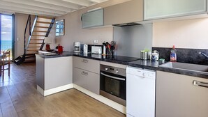 Una cocina moderna con horno integrado, lavavajillas y un amplio ventanal con vistas al mar.