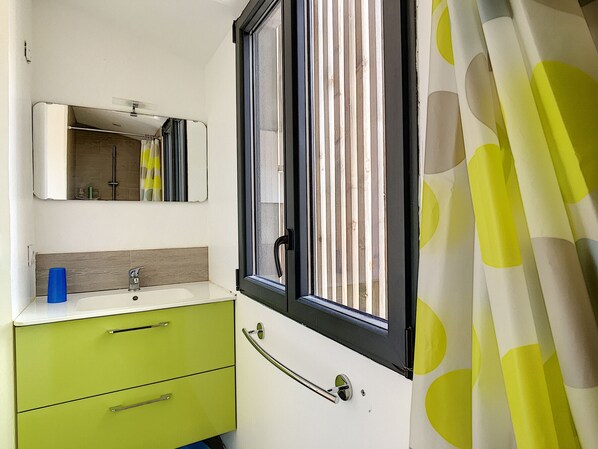 Un baño con ventana, espejo, lavamanos y un mueble verde.