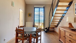 Un comedor con mesa y sillas, una escalera y vistas a la playa.