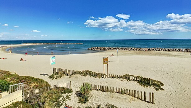 Una playa con una cerca de madera, un letrero y un litoral rocoso.