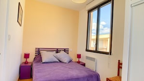 Un dormitorio con una cama, dos mesitas de noche, una silla, un ventanal y un calentador de pared.