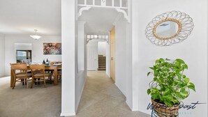 A dining area with a wooden table and chairs, a painting on the wall, and a hallway leading to a staircase. - Sellicks Seascape by Wine Coast Holiday Rentals (SELLICKS BEACH)