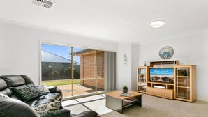 A living room with a leather sofa, a coffee table, a TV stand with a screen, and a sliding glass door leading to a patio. - Sellicks Seascape by Wine Coast Holiday Rentals (SELLICKS BEACH)