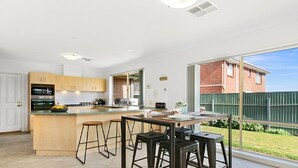 A modern kitchen with a central island, bar stools, and a large window overlooking a backyard. - Sellicks Seascape by Wine Coast Holiday Rentals (SELLICKS BEACH)
