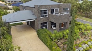 Ein zweistöckiges Haus mit überdachter Garage, Balkon und einem gepflegten Garten mit verschiedenen Pflanzen.