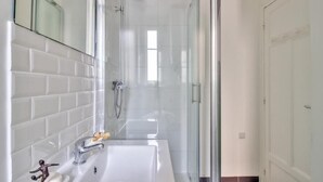 Et moderne badeværelse med en glasvæg omkring brusenichen, en hvid vask med sæbeskål og et spejl over vasken.