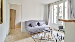 Et moderne, lyst rum med en grå sofa, et lille rundt bord og udsigt ud ad store vinduer.