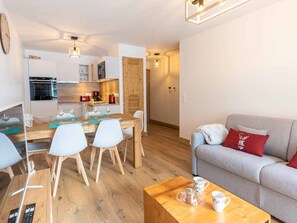 A modern living room with a grey sofa, a wooden coffee table, and a dining area with a wooden table and chairs. - Apartment for 6, 2 bedrooms, balcony, parking, WIFI (Valmorel)