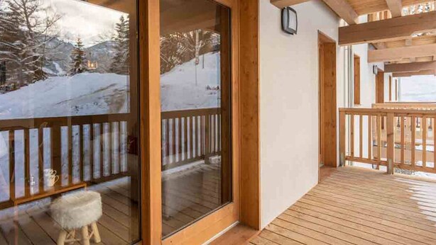 Une terrasse en bois avec une porte vitrée donnant sur un paysage enneigé.