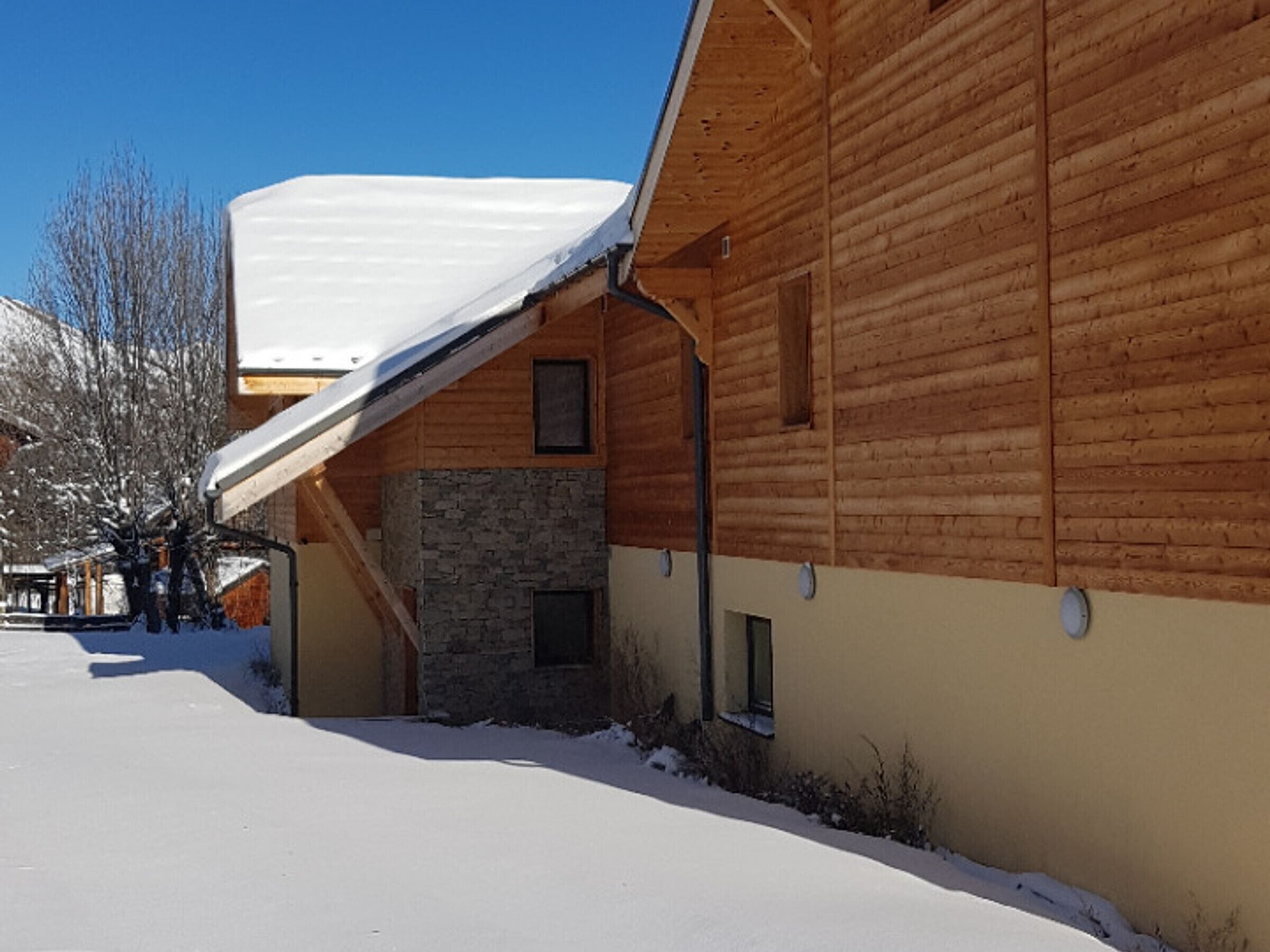 A wooden building with a stone wall and a snow-covered roof.