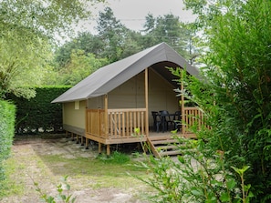 A small, single-story wooden cabin with a balcony, surrounded by dense greenery.