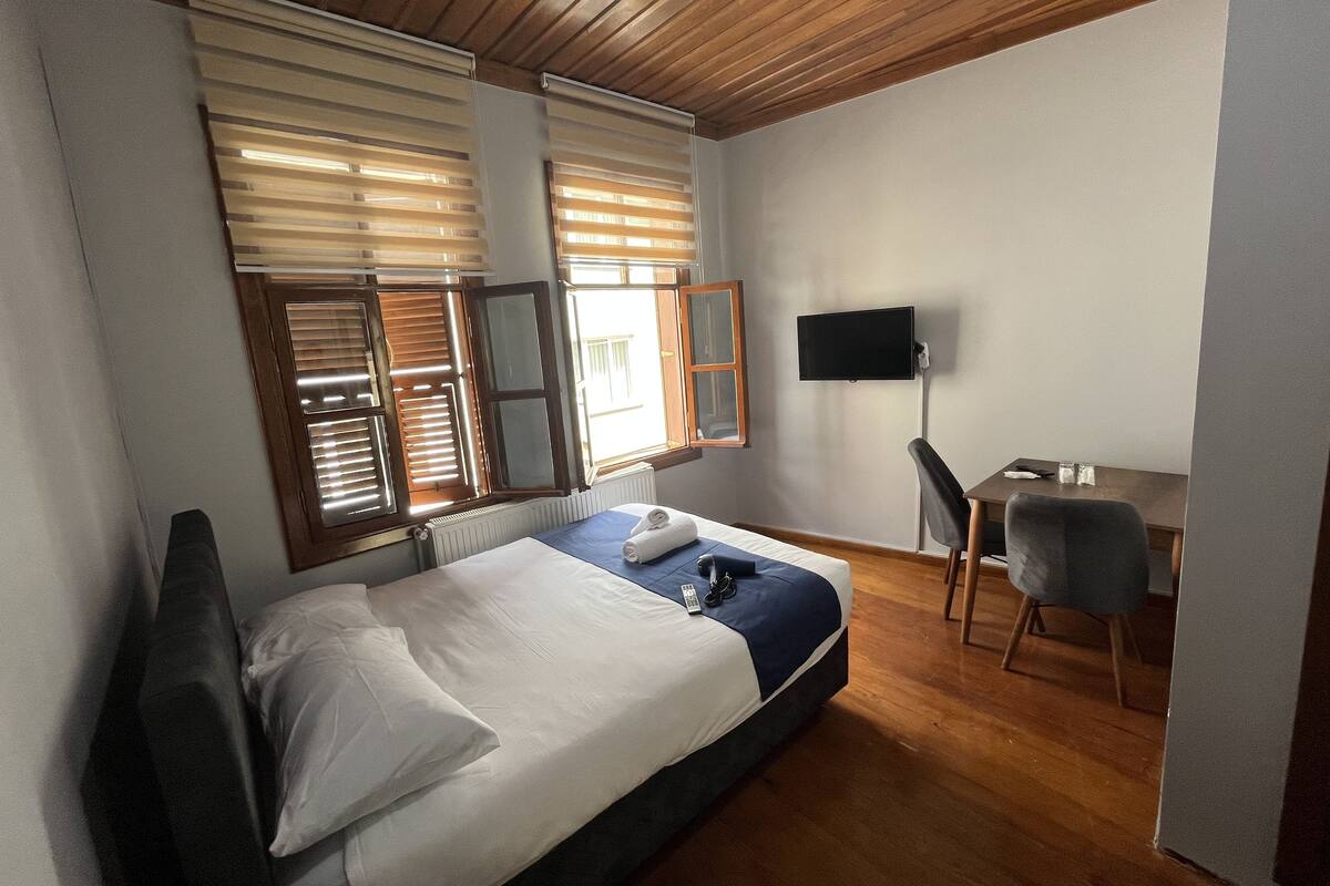 Un dormitorio con cama, escritorio, silla, televisión y ventana con persianas.