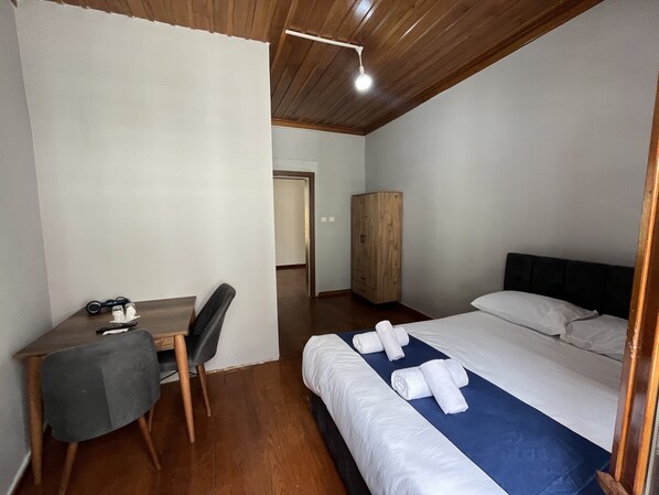 A hotel room with a wooden desk, a chair, a bed with white linens and towels, and a wardrobe.