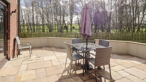 A patio area with a table and chairs, a covered umbrella, and a view of a fenced field with trees. - Mill End (Penrith)