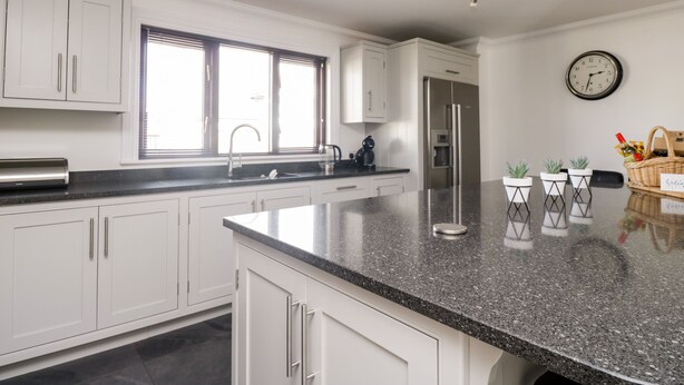 A modern kitchen with white cabinetry, a granite countertop, stainless steel appliances, and a clock on the wall. - Mill End (Penrith)