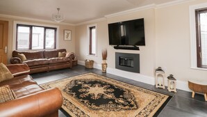 A living room with a leather sofa, a large rug, a fireplace, and a mounted TV. - Mill End (Penrith)