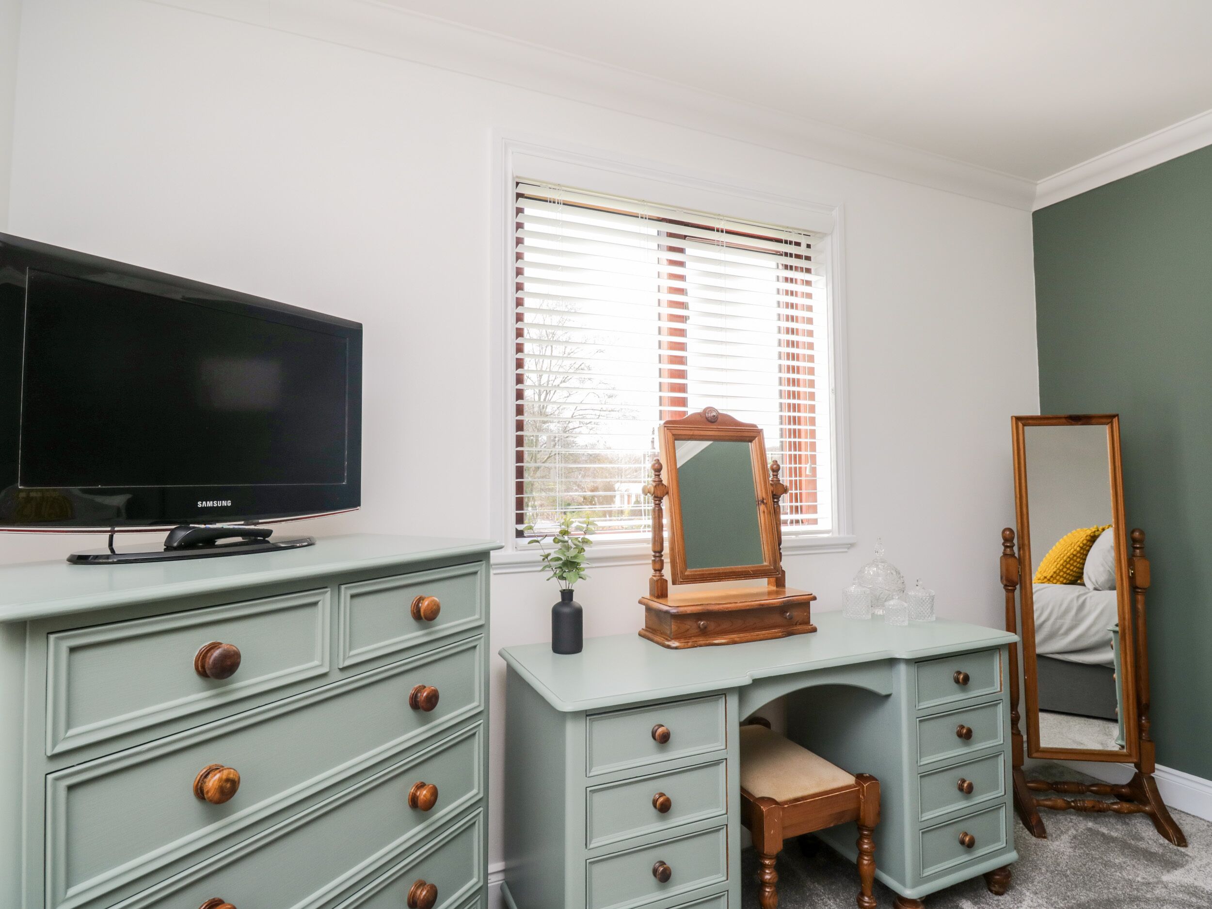 Quarto com televisão, penteadeira, espelho e cama.
