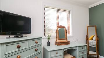 Quarto com televisão, penteadeira, espelho e cama.