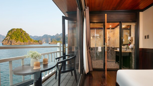 A balcony with a table, chairs, and a view of a green island across the water. - Arcady Boutique Cruise (Tuan Chau)