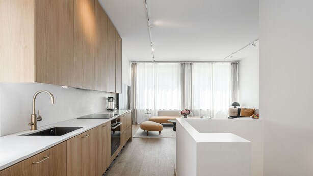 Una cocina moderna con armarios de madera, una encimera blanca y un horno empotrado.