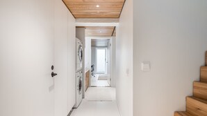 Un pasillo estrecho con techo de madera, una lavadora y una escalera a la derecha.