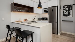A modern kitchen with white cabinetry, a central island with bar stools, a black pendant light, and a stainless steel refrigerator.