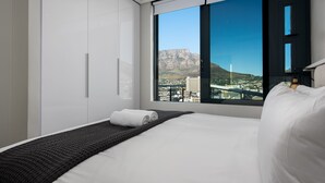A modern hotel room with a large bed, a view of a cityscape and mountains, and a large window.