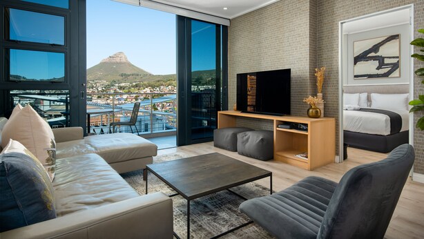 A modern living room with a large TV, comfortable seating, a bookshelf, and a view of a mountain and town.