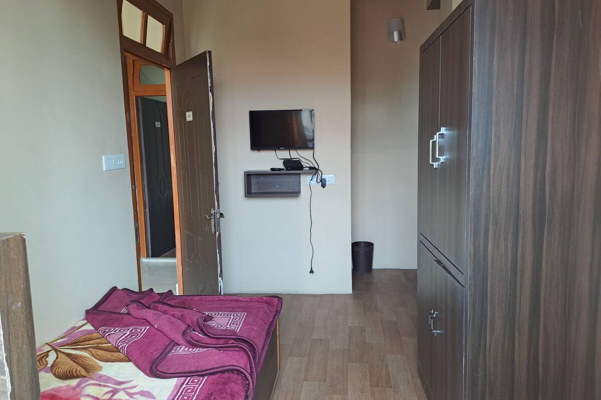 A room with a bed, a wardrobe, a television mounted on the wall, and a door leading to another room.