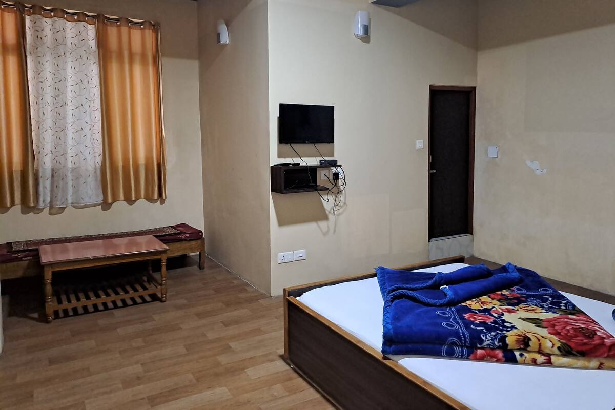 A bedroom with a bed, a desk, a chair, a television, and a door.