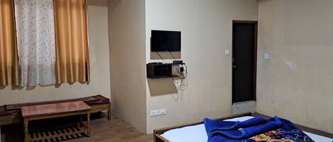 Un dormitorio con cama, escritorio, silla, televisor y puerta.