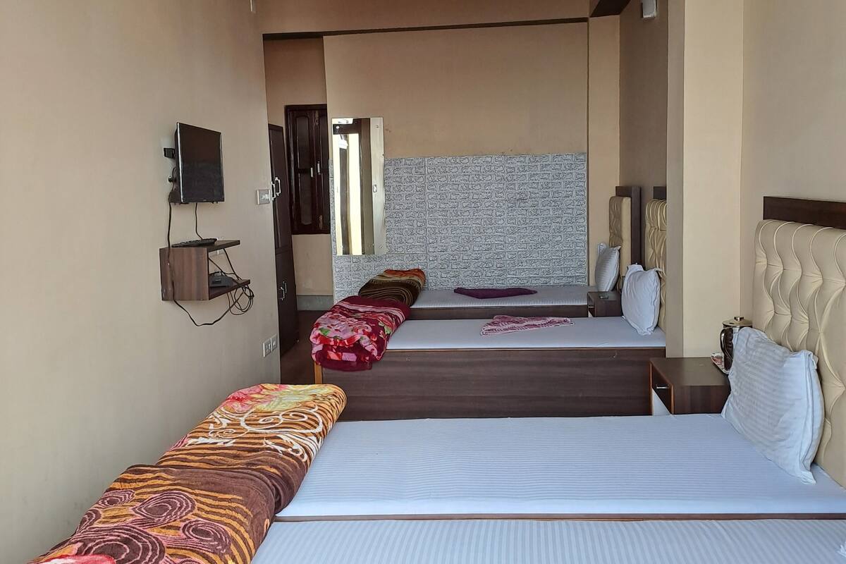 A hotel room with three beds, a television, and a patterned wall.