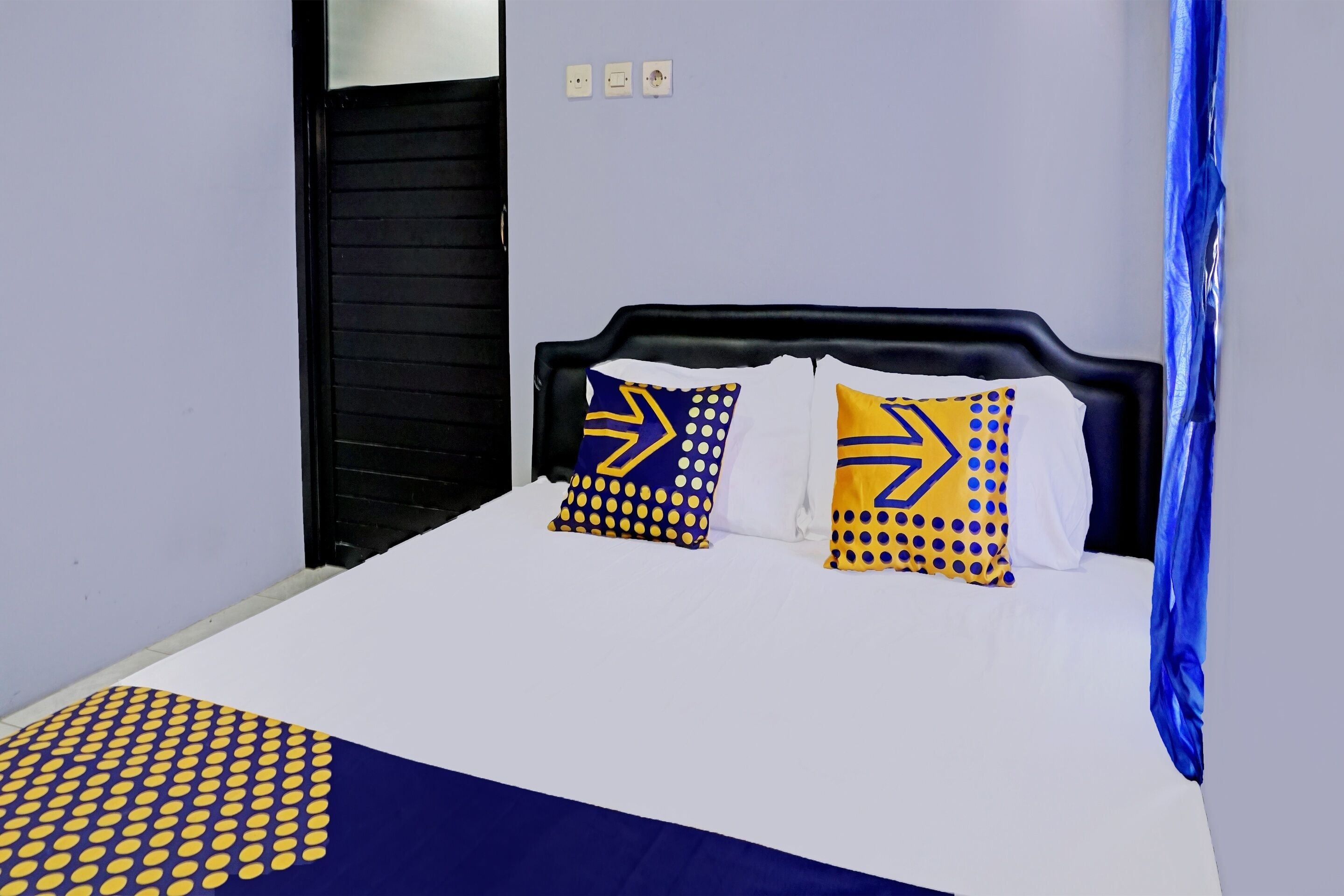 A bed with a white and blue bedspread, two pillows with yellow and blue patterns, and a black headboard.