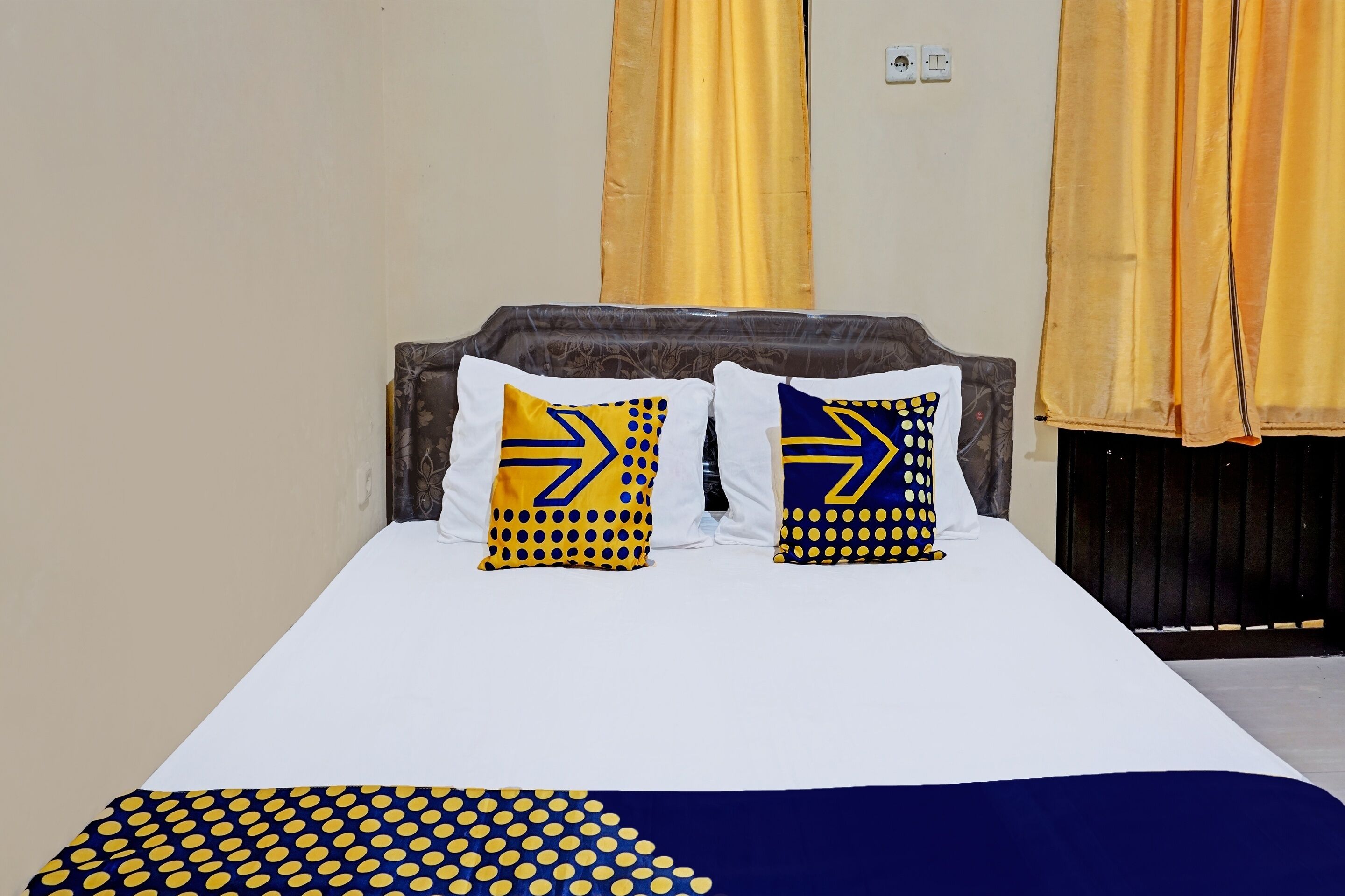 A bed with two pillows featuring geometric patterns, a white bedspread, and a blue and yellow polka dot blanket.