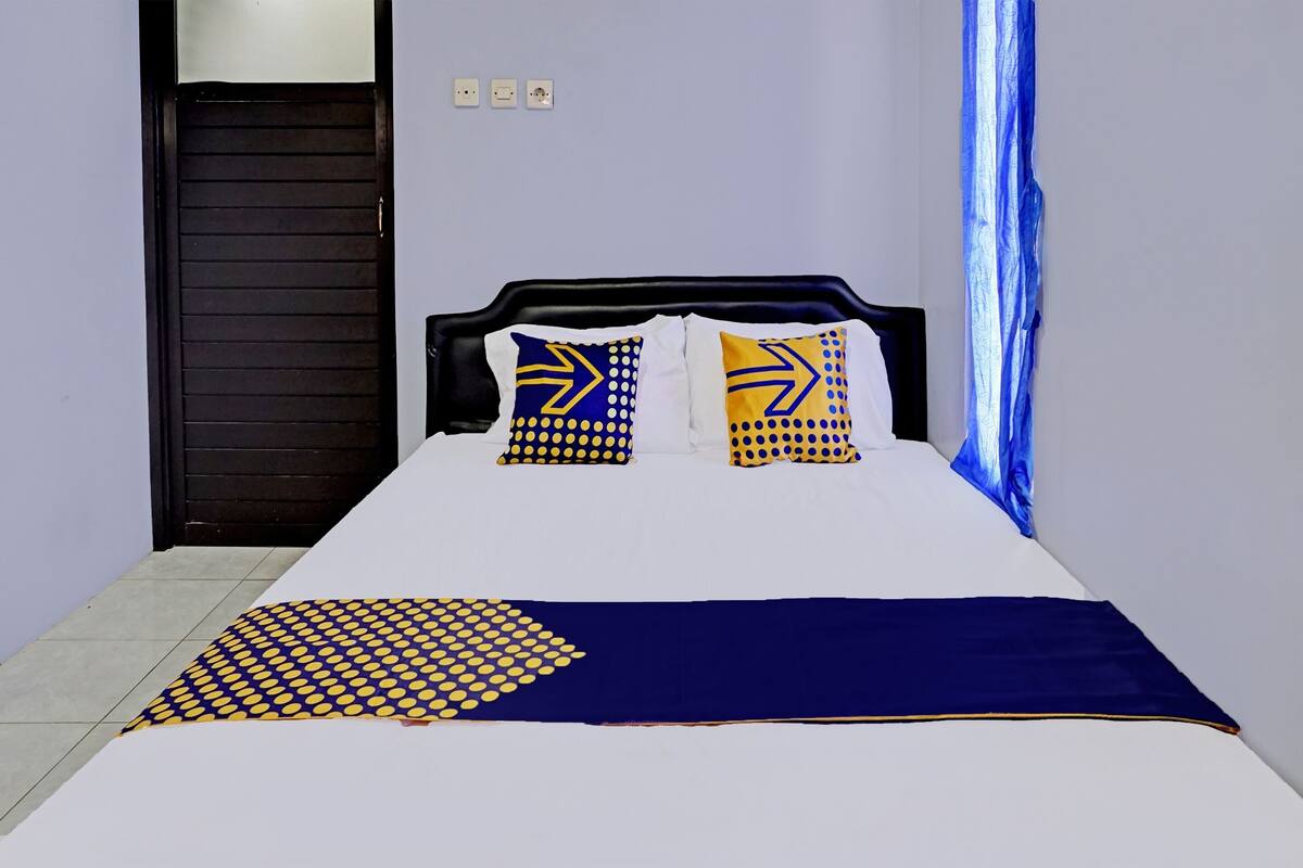 Una cama con colcha blanca y azul, dos almohadas con diseños geométricos y un plaid azul oscuro.