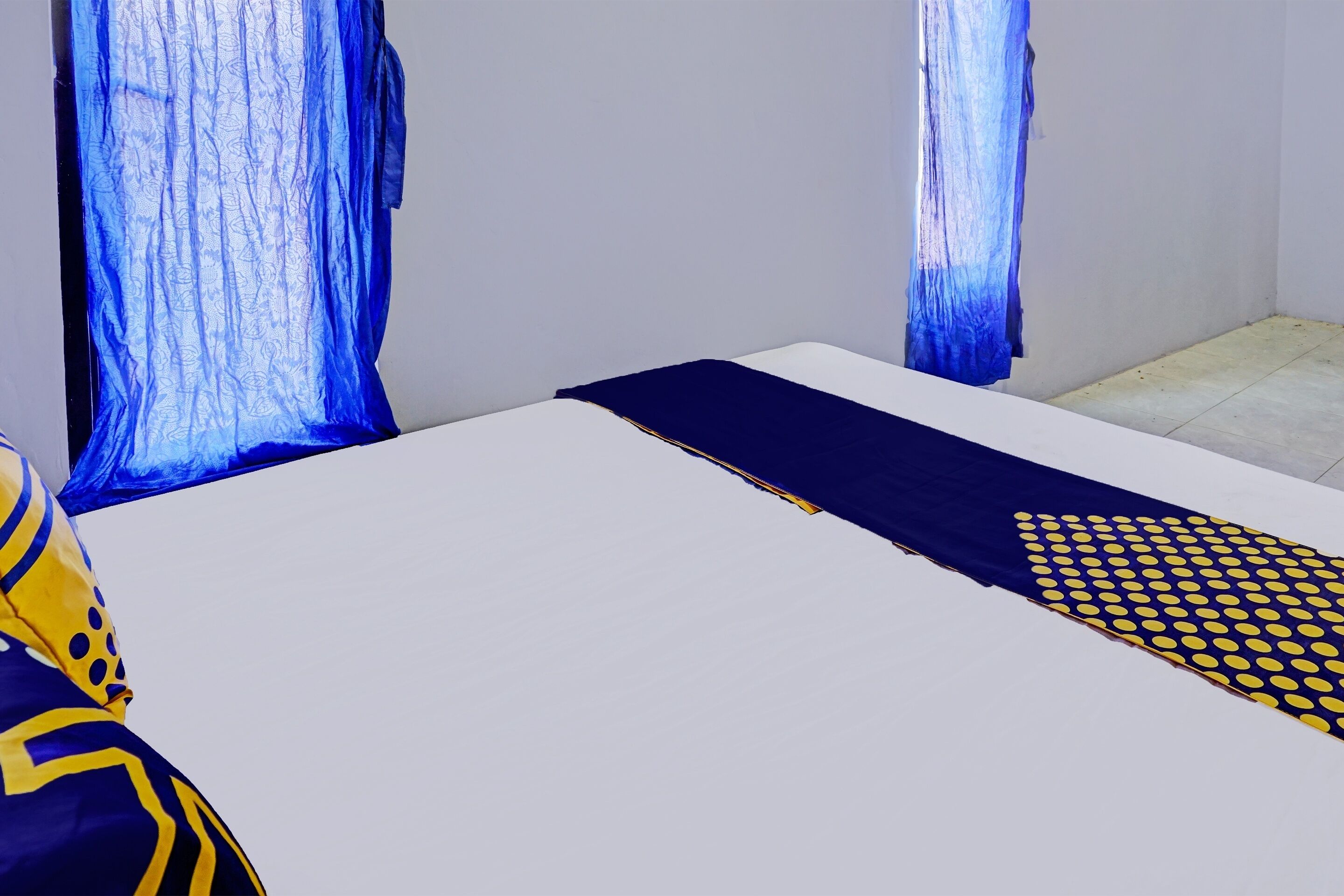 A room with a bed, a blue and yellow patterned bedspread, and sheer curtains.