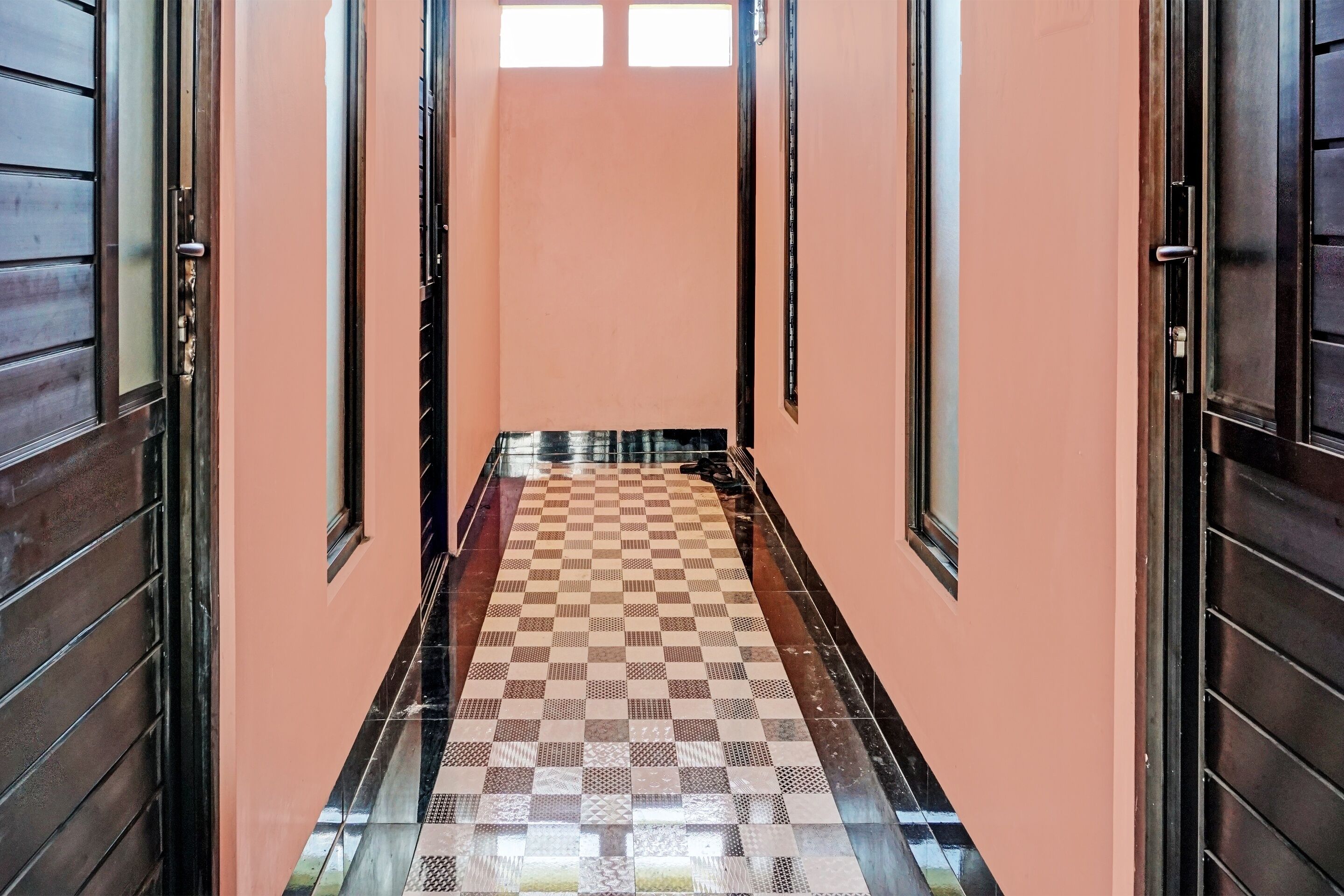 A hallway with a checkered floor pattern, peach-colored walls, and wooden doors with metal handles.