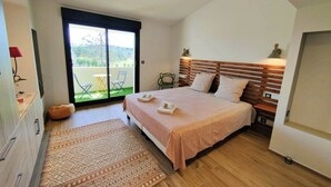 Una camera da letto con un letto grande, una testata in legno, un tavolino con una lampada e vista su un balcone con sedie.