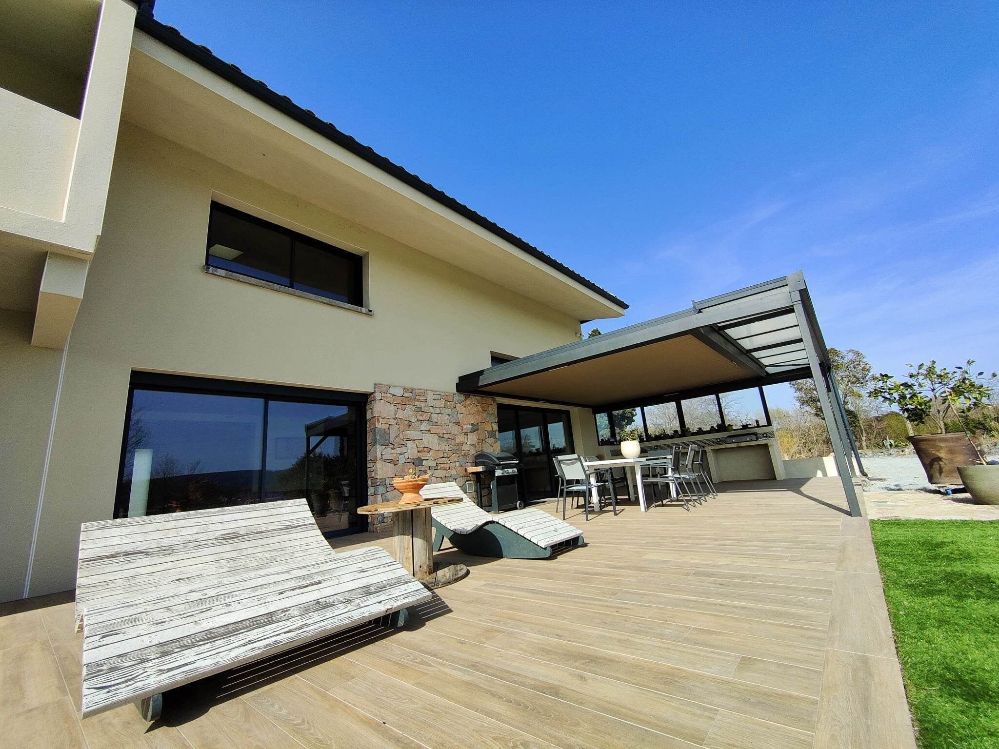A modern house with a patio, outdoor seating, and a barbecue area.