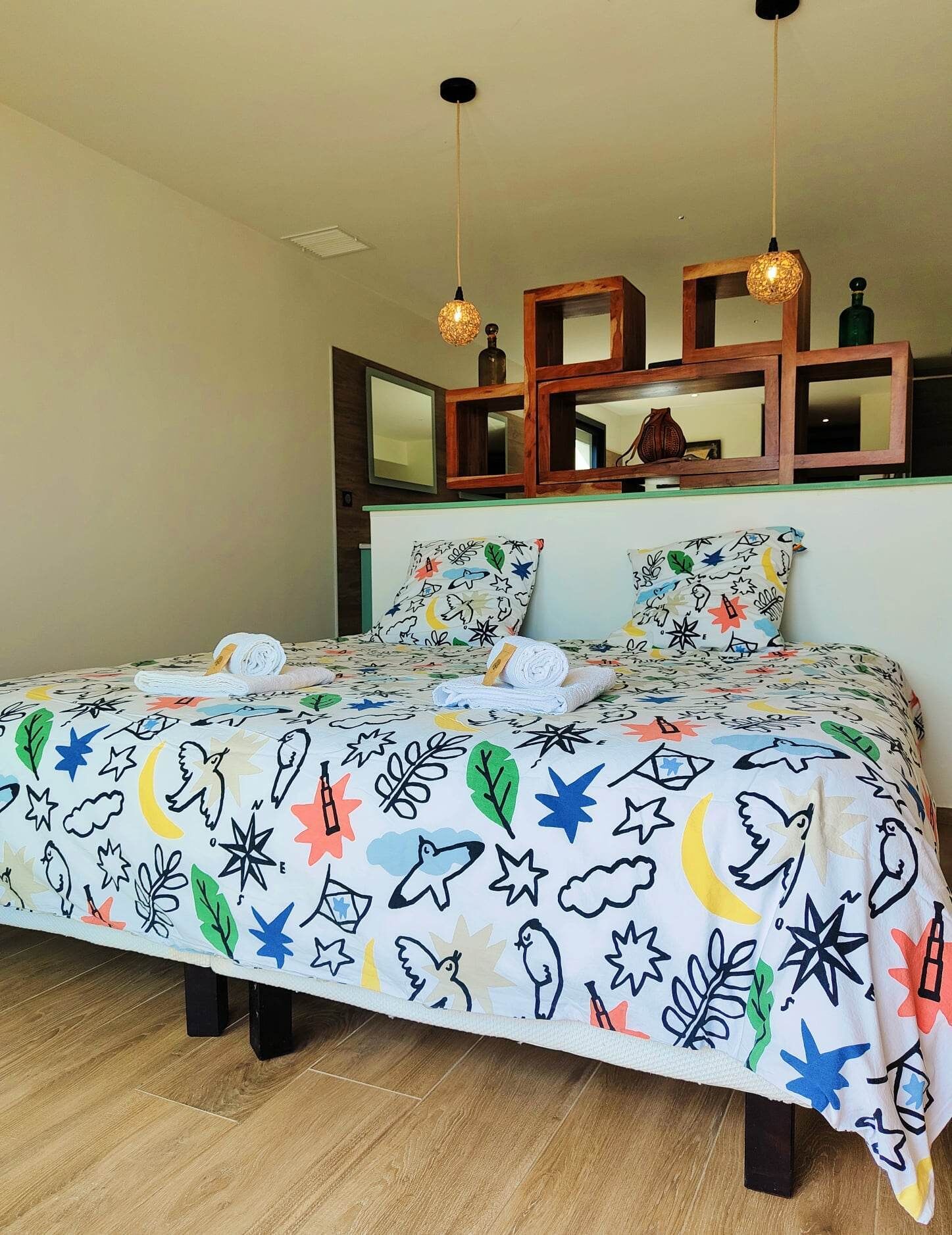 Une chambre à coucher avec un lit, deux luminaires suspendus, un miroir et une étagère en bois.