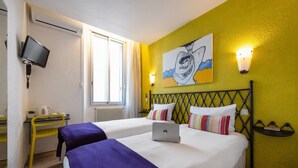Habitación de hotel con dos camas, un escritorio, una silla, un televisor y un cuadro en la pared.