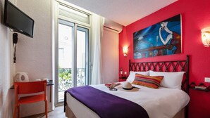 Habitación de hotel con una cama, un escritorio, una silla, un televisor y un cuadro en la pared.
