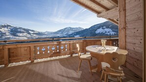 A wooden deck with a table and chairs, overlooking snow-covered mountains.